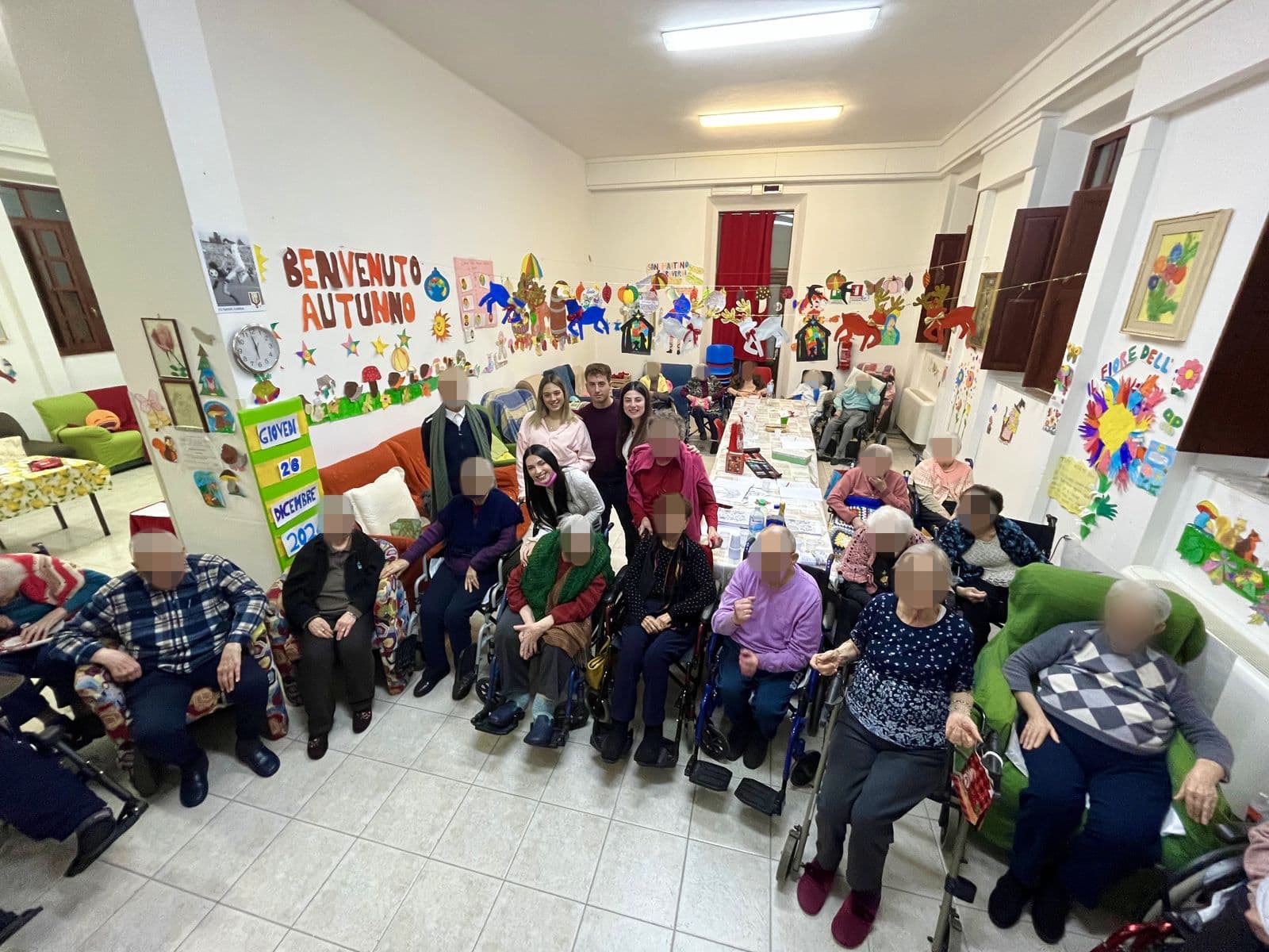 Ospiti e volontari riuniti nel salone della struttura, decorato con i lavoretti per la festa